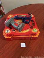 Orange Beyblade Burst stadium with gray and blue launchers on top shown on wooden table.