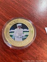 Gold plated Princess Diana commemorative coin with photo of Diana in white naval uniform, circular coin sealed in plastic capsule.