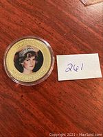Gold-plated collectible coin featuring Princess Diana's portrait in the center, encased in a clear round protective capsule. The coin has inscriptions on the gold-plated rim.