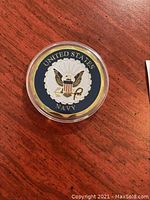 US Navy emblem side of gold plated challenge coin in capsule on wooden surface