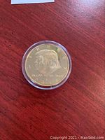 Gold plated Trump coin in protective capsule showing obverse with Trump's profile and inscriptions including LIBERTY, IN GOD WE TRUST and year 2018.
