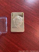 Front of rectangular gold plated commemorative coin showing raised portrait relief of Margaret Thatcher with 'The Iron Lady' text.