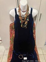 Full view of a mannequin wearing a dark blue velvet dress showcasing multiple layered beaded necklaces and a bracelet laid in front