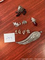 Overview of all nine pendants arranged on a red wooden surface including lizard, elephant, letters, wing, and drop pendant.