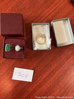 Three rings displayed in two open boxes on a wooden surface with a handwritten number label '308'.