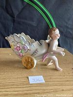 Side view showing the cherub pulling the wheelbarrow-style planter with floral decoration and yellow wheels.