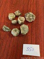 Seven raw green apatite mineral specimens displayed on a wooden surface with a small paper numbered 351.