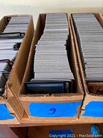 Three cardboard boxes packed with large quantities of Magic: The Gathering cards.