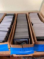 Three cardboard boxes filled with a large number of Magic: The Gathering cards.