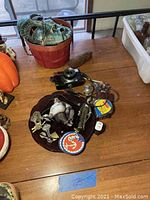 Overview photo showing voodoo mask on red basket, black vintage Konica camera, and various small collectibles arranged on a glass plate on wooden table.