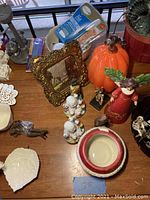 Overview of various items on a table showing figurines, ceramic pumpkin, framed artwork, plate pieces, and small miscellaneous decorative objects.