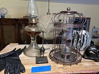 Photo of brass oil lamp, metal birdcage, crane statue, black gloves, and black cat statue on wooden surface