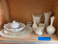 White porcelain Lenox serving and decorative items arranged on wooden shelf.