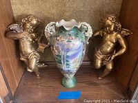 Front shot showing two cherub figurines flanking a large Japanese vase with raised enamel and painted nature scenes.
