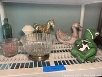 Green vintage glass bottle, white ceramic vase, gold metal horse, ceramic duck, frog decoration on shelf
