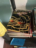 Stack of comic books topped with 'Out of the Storm' comic book featuring a character surrounded by lightning effects on the cover.