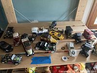 Top down view of approximately 16 model cars of various styles placed on wooden surface showing scratches and use signs.