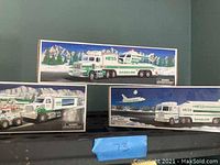 Photo showing all three Hess collectible trucks with packaging boxes in the background and numbering label '73'.