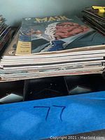 Side view of the pile of approximately 20 comic books showing the spines and some edge wear.