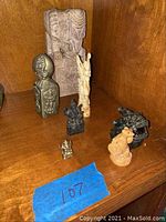 Seven small figurines including bronze Ganesha, elephant carving, and various totem/statue pieces arranged on wooden surface.