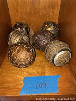 Six decorative balls arranged on a wooden shelf, showing different intricate textured and embossed patterns.