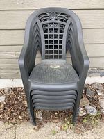 Stack of six black plastic outdoor lawn chairs with lattice and floral design on backrests.