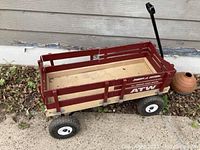 Red Radio Flyer All-Terrain Cargo Wagon positioned on a cement area against a house wall.