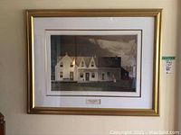 Full view of gold framed lithograph art by A.J. Casson depicting a farmhouse scene with buildings and figure, behind glass and double matted.