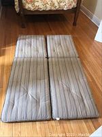 Pair of long outdoor cushions laid on hardwood floor, showing full length and tufted striped canvas fabrication.