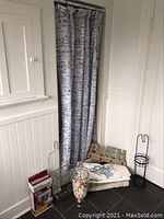 Packed corner view showing bath towels, jar of sea shells, toilet repair set in box, toilet paper holder, bath-themed wooden letters 'BATH', and metal hooks leaning against wall near shower curtain.