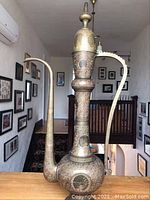 Full tall view of the large vintage brass coffee pot with intricate design and lid, showing curved spout and handle.