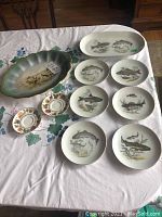 Photo of the full set showing 1 large scalloped grouse-themed oval platter, 6 fish-themed side plates, and 2 teacups with 2 saucers.