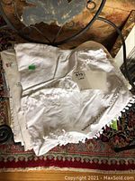 Stack of white and cream-colored table linens showing lace and embroidered edging, including napkins and tablecloths.