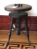 Front angled view of the vintage wooden piano stool showing claw foot legs, circular seat, and detached strut piece atop the seat.
