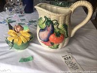 Basketweave pitcher with vegetables and decorative teapot on table with lot tag