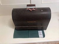 Closed vintage Singer sewing machine case with a curved top and handle on a green cloth.