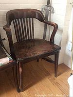 Front and angled view of the vintage oak office chair showing curved arms, slatted backrest, and worn seat surface.