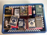 Basket full of various vintage playing decks showing assorted brands and types including Bicycle, Vogue, Plastalac, and trivia challenge cards.
