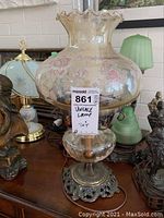 Full view of vintage oil-lamp style table lamp showing floral decorated glass shade and ornate metal base.