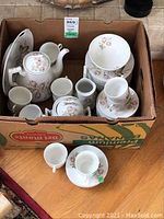 Full set packed inside a cardboard box showing coffee pot, cups, saucers, sugar bowl, creamer and side plates with floral design.