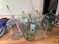 Six carboys on wooden surface with long white stirring spoon inside one