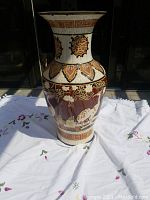 Full front view of vintage East Asian motif vase on a white embroidered cloth with floral designs.