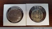 Photo of the front (reverse) sides of the two coins, showing the canoe design on the one dollar coin and the coat of arms on the fifty cent coin.