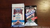 Photo of two unopened Upper Deck hockey card packs on a wooden surface. Left pack is the 1991-92 Jumbo pack in white, blue, and red packaging. Right pack is the 1990-91 NHL High Series pack in black, white, red, and blue packaging.