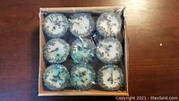 Top view of nine white votive candles with blue glitter decoration inside a square cardboard box.
