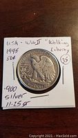 Front side of 1945 Walking Liberty U.S. half dollar coin showing eagle design with inscriptions and notes about silver content and weight on paper holder.