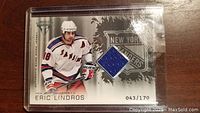 Front view of 2004 Titanium Eric Lindros hockey card showing player image, team logo, and embedded blue fabric swatch.