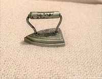 Side view of miniature cast iron sad iron showing triangular base and textured grip handle with wear.