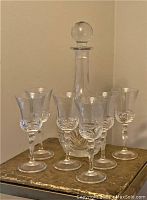 Full set view showing decanter with stopper and six wine glasses arranged around it on a gold-toned surface, highlighting the cut crystal patterns and clarity.