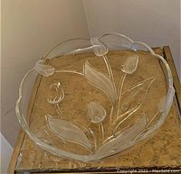 Top-down view of large clear glass serving dish showing floral etching with tulips and leaves on glass surface and scalloped rim.
